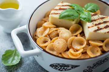 Close-up of orecchiette pasta with grilled cheese and fresh green basil, selective focus