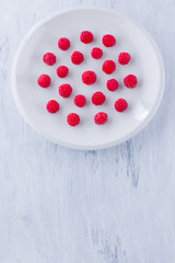 Raspberries on a white plate. Red raspberry berries on a white background. Berries for vegan. Summer concept. Minimalistic food. Top view. Copy space