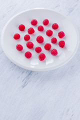 Raspberries on a white plate. Red raspberry berries on a white background. Berries for vegan. Summer concept. Minimalistic food. Top view. Copy space
