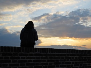 One Single Woman Silhouette Sitting on Brick Wall during Sunset with Cloudy Sky in Background