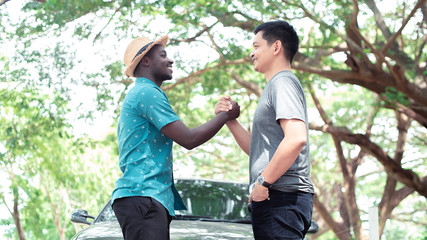 Naklejka na ściany i meble African man and asian man shaking hands over a deal with car and green natural background