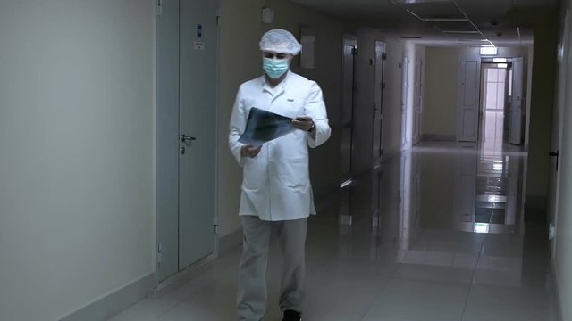 doctor in uniform walks down the hallway stops looking at the X-ray in the hallway of the clinic X-ray study