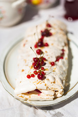 Meringue roll with fresh berries - cherry and red currant - on white plate