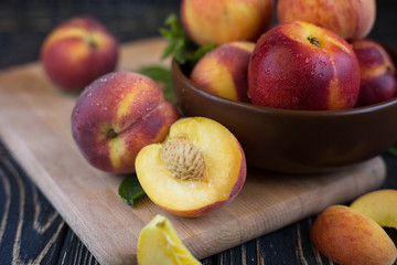 Delicious juicy orange-red peaches and nectarines on a dark background in a clay bowl. Dark background, still life of ripe summer fruits on a brown wooden table. Close-up