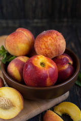 Delicious juicy orange-red peaches and nectarines on a dark background in a clay bowl. Dark background, still life of ripe summer fruits on a brown wooden table. Vertical photo