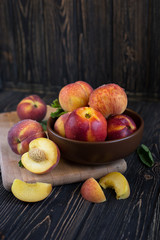 Delicious juicy orange-red peaches and nectarines on a dark background in a clay bowl. Dark background, still life of ripe summer fruits on a brown wooden table. Vertical photo