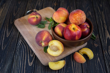 Delicious juicy orange-red peaches and nectarines on a dark background in a clay bowl. Dark background, still life of ripe summer fruits on a brown wooden table.