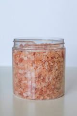 Himalayan salt. Bath salts. Spa treatment. The industry of beauty and relaxation. Scattered salt on a white background. Bath crystals in a clear jar. Orange, pink. Packaging.