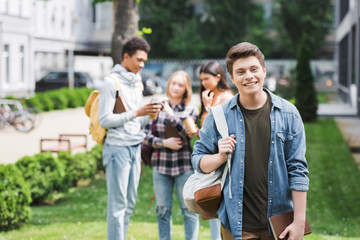 Smiling teenager holding book and backpack and looking at camera