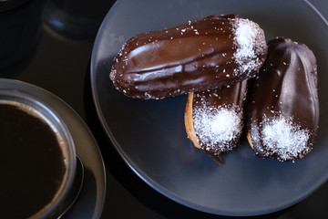 three chocolate eclairs on a plate and cup of coffee. traditional fcench Chocolate Eclairs