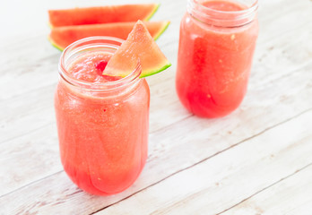 Watermelon smoothies in a glass filled with watermelon on top in a wooden background
