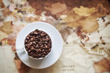 roasted coffee bean in white coffee cup on vintage world map