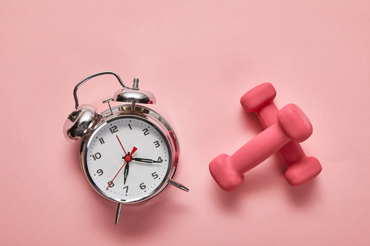 top view of silver alarm clock and pink dumbbells on pink background