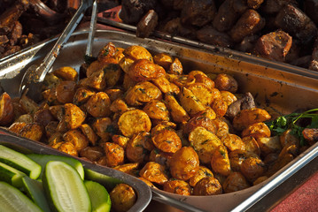 Roast potatoes in a large pan. Delicious food at the festival. Many potatoes on the table in a metal tray.