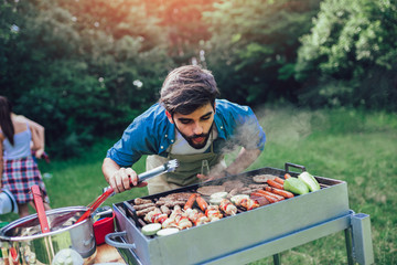 Naklejka na ściany i meble Handsome male preparing barbecue outdoors for friends