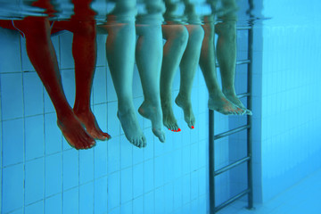four people legs underwater in the swimming pool. Party. Summer. Vacation, diversity, friendship and sport concept.