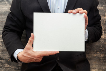 man in a suit with a blank white sign. Wooden wall background.