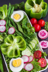 A set of vegetables with egg: peas, green pepper, radishes, lettuce, tomatoes. Black background.