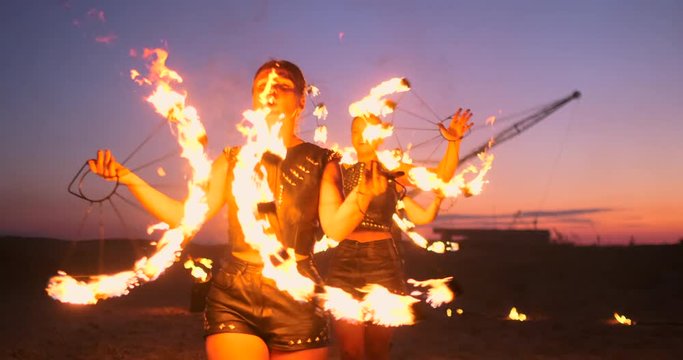 Professional artists show a fire show at a summer festival on the sand in slow motion. Fourth person acrobats from circus work with fire at night on the beach.