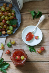 Gooseberry marmalade in a glass jar and gooseberry berries on a wooden table. Rustic style.