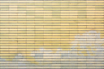 Old yellow tiled brick surface with washed out graffiti on the lower part