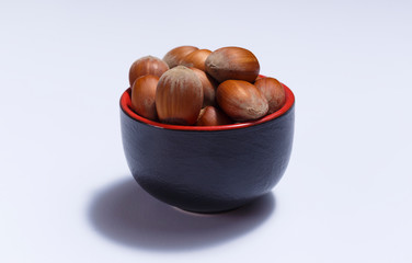 Front view of hazelnuts inside a red bowl isolated on white background.