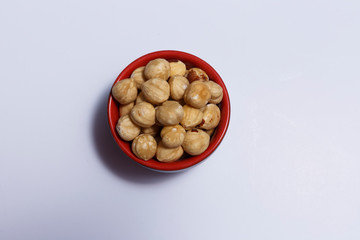 Top view of hazelnuts inside a red bowl isolated on white background.