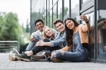 Happy friends smiling, sitting and taking selfie with smartphone