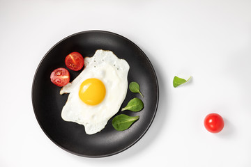 Fried eggs with fresh lettuce and tomatoes on a black plate. Isolated on white background.