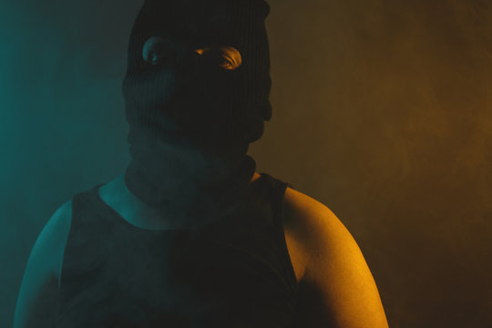 Portrait of relaxed man in black balaclava, illuminated from abstract light in green and yellow colors