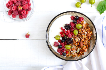 Yogurt, granola, fresh berries in a bowl on a white wooden background. Delicious and healthy breakfast. Proper nutrition. Dietary menu. The top view, flat lay