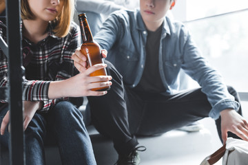 cropped view of boy giving glass bottle of beer to blonde girl