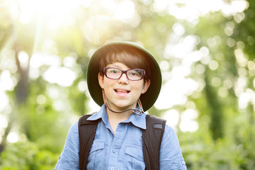 Fototapeta na wymiar Portrait of little explorer in forest. Boy traveler in helmet play in the park. Happy child in glassas go hiking with backpack in summer nature. Dream concept.