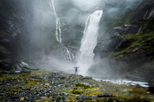 Figure standing in front of a raging waterfall in Zealand