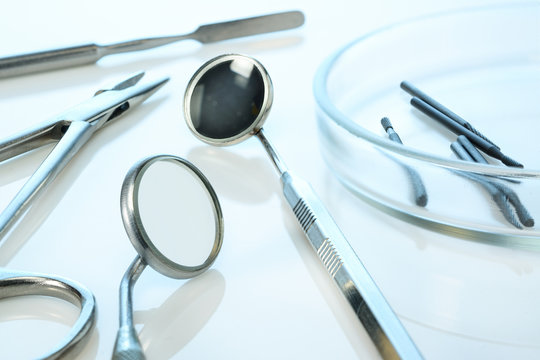Dentist equipment: dental mirrors, spatula, kornzange or forceps, dental burs in Petri dish. Dental tools on blue glossy surface, closeup.