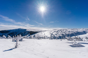 View of a winter mountain landscape of Krkonose National Park, Czech Republic, with famous mountain hut Labska bouda. Sunstar, bright ble sky and snow covered mountain landscape of Giant Mountains.
