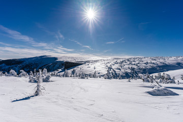 View of a winter mountain landscape of Krkonose National Park, Czech Republic, with famous mountain hut Labska bouda. Sunstar, bright ble sky and snow covered mountain landscape of Giant Mountains.