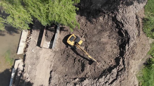 Excavator digging soil and loading dump truck tipper at excavation site aerial static