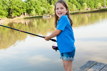 Cute  child girl  fishing from wooden pier on a lake. Family leisure activity during summer sunny day.  little girl having fun by a river at beautiful summer evening