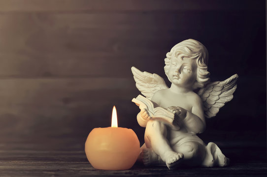 Angel and white candle on dark background