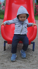 Fototapeta na wymiar Little boy having fun on a playground outdoors in summer. Toddler on a slide.