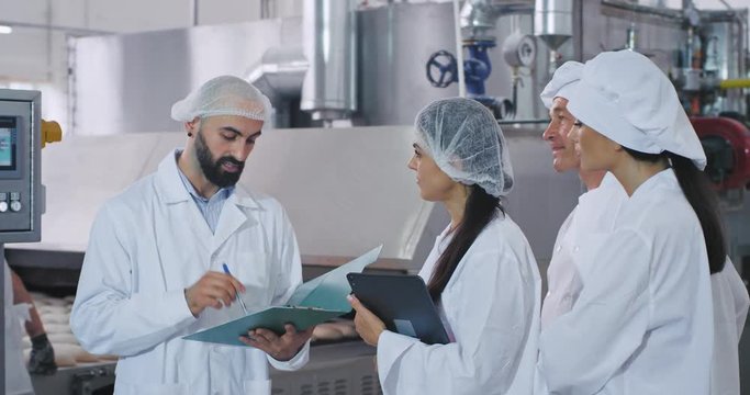 Bakery industry man engineer his assistance and baker chef and young baker lady have a meeting , man engineer explaining something on the map while he holding in hands background big manufacturing