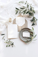 Summer wedding stationery mock-up scene. Blank greeting cards, envelope, vintage silver plate, olive branches and ribbon. White background with cotton table runner in sunlight. Flat lay, top view.