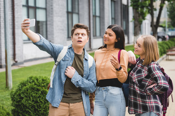 happy teenagers holding smartphone, taking selfie and smiling