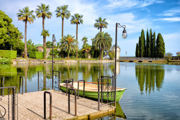 pond in tropical city park with wooden boat moored to pier wide scenic landscape view of lake water on green palm tree nature background tourist vacation beautiful landmark