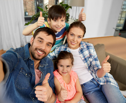 family and people concept - happy father, mother, little son and daughter taking selfie and showing thumbs up at home - Powered by Adobe