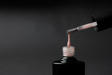 beige nude shellac nail polish dripping on black background with copy space