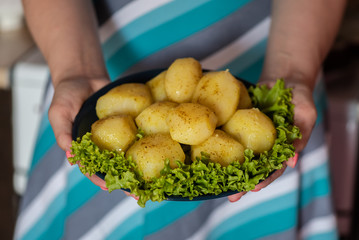 Prepared boiled potatoes with spices and a lettuce green leaves on a plate in a woman hands.