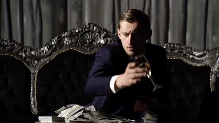 Business life concept. Cash, money, banknotes on table. Man in suit, businessman sit in dark luxury interior background. Macho with strict face celebrate success with champagne, achievement, profit.