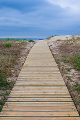 Vertical view of wooden path towards the beach with sea and cloudy sky in the background in Cantabria, Spain, Europe